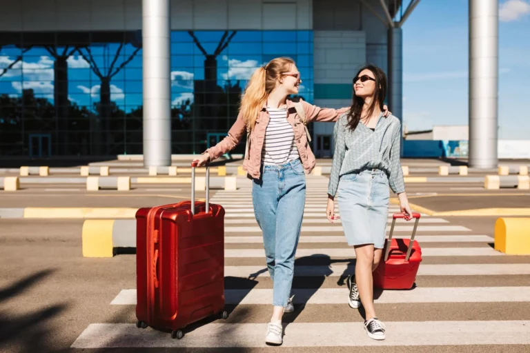 beautiful-stylish-girls-sunglasses-happily-walking-along-pedestrian-strip-with-red-suitcases-airport-background